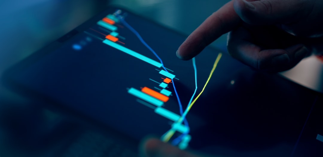 A close-up of a tablet displaying trading charts with a finger pointing at the screen